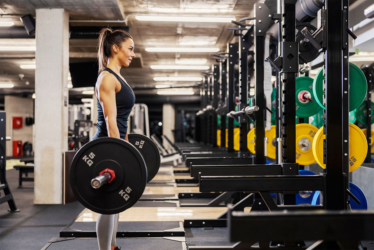 Woman With Ponytail in a Black Tank Top and Grey Leggings Deadlifting 5 KG Weights